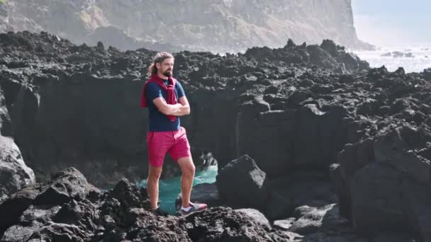 Hombre con pantalones cortos rojos de pie sobre una roca volcánica — Vídeos de Stock