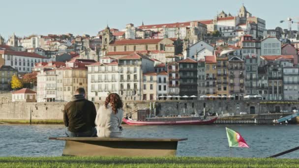 Porto, Portugal. Par sitta på en bänk vid floden njuter av charmig utsikt över staden — Stockvideo