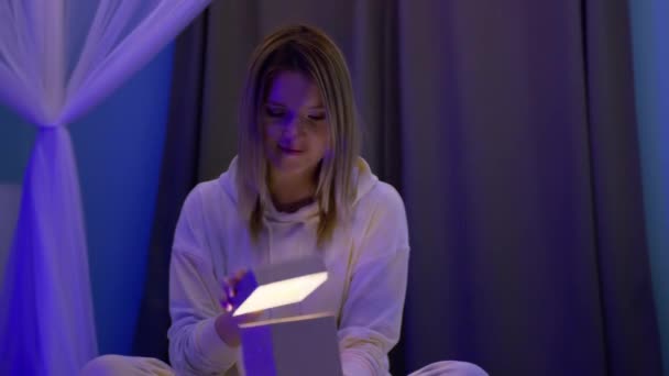 Overrasket smilende kvinde åbner gylden glitter gaveæske med magisk lys inde 8K – Stock-video