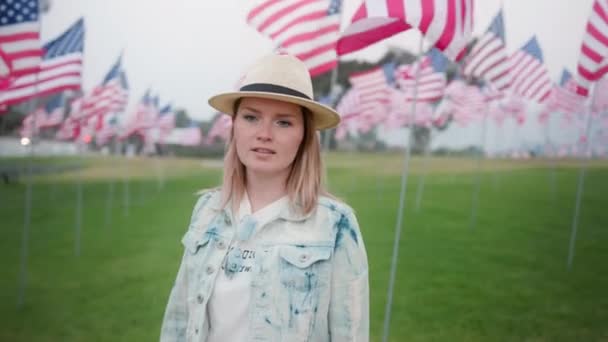 Retrato de calma jovem caminhando no parque verde entre acenando bandeiras americanas — Vídeo de Stock