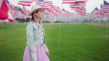 Kentsel yeşil parktaki genç kadın. Rüzgarda dalgalanan Amerikan bayrak direkleri.