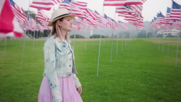 Jonge vrouw in het stedelijke groene park met veel Amerikaanse vlaggenmasten die in de wind waaien — Stockvideo