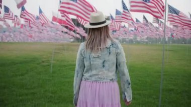 Anma parkındaki kadını izleyen kamera. 4K rüzgarıyla pohpohlanan bir sürü Amerikan bayrağı.