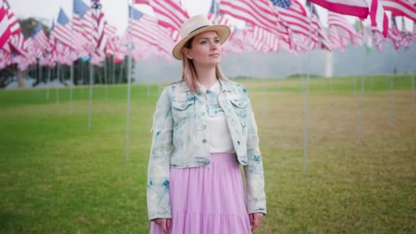 Jeune femme attrayante profitant de soirée dans un parc commémoratif avec des drapeaux américains 4K — Video