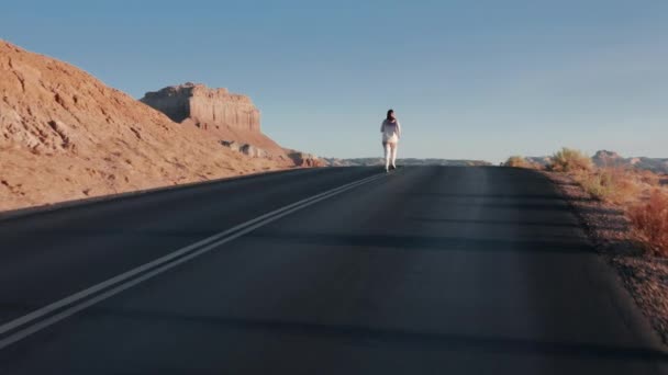 Drohne fliegt tief über Straße und verfolgt Frau, die durch filmische Sonnenaufgangswüste läuft — Stockvideo
