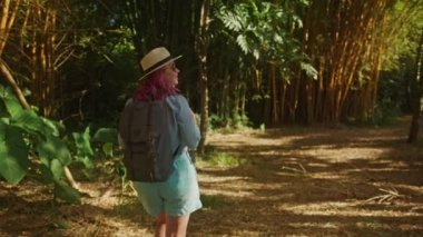 Kamera pembe saçlı kadını yeşil bambu ormanında doğa macerası gezisinde takip ediyor.