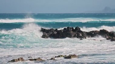 Dalgalar ağır çekimde deniz taşlarına çarpıyor, dalgalı okyanus suları, güneşli yaz günü