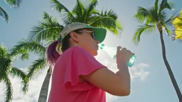 Kobieta pije wodę, relaksując się na świeżym powietrzu w tropikalnym parku w letni słoneczny dzień 4K — Wideo stockowe