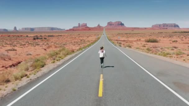 Filmisk antenn atletisk kvinna som kör på motorvägen till Monument Valley, natur 4K — Stockvideo