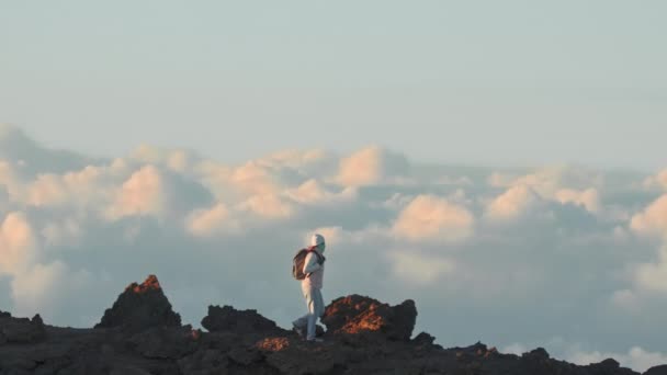 Мандрівник досліджує високу гірську вершину над хмарами на заході сонця, повільний рух 4K — стокове відео