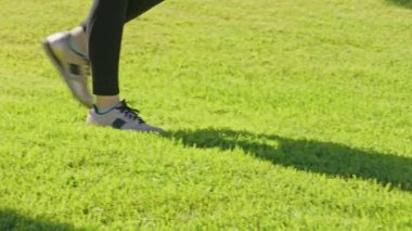 Spor ayakkabılı kadın ayaklarının parkta canlı yeşil çimlerin yanından geçişi.