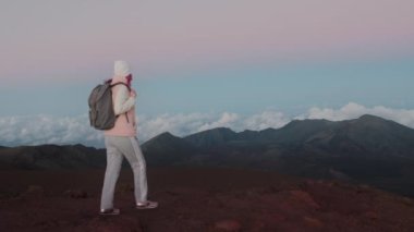 Maui volkanı üzerinde pembe günbatımında arka planda sinematik bulutların keyfini çıkaran kadın. 