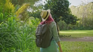 Güzel gezgin kadın pembe saç stiliyle botanik bahçesinde yürüyor.