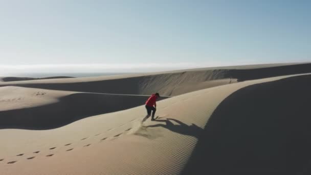 Hombre corriendo energéticamente por las dunas creando nubes doradas de arenas al atardecer 4K — Vídeos de Stock