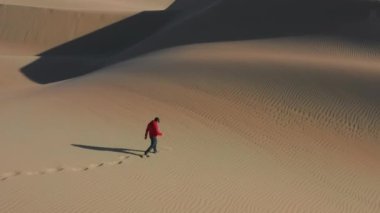 Adam enerjik bir şekilde kum tepelerine doğru koşuyor gün batımında altın kum bulutları yaratıyor. 4K