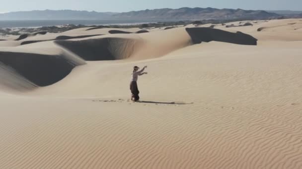 Mulher usa um fone de ouvido realidade virtual e controladores, dançando em dunas de areia 4K — Vídeo de Stock