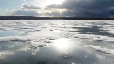 Donmuş gölün üzerinde uçan dron eriyen buzla, güneş bulutları günbatımında yansıyor.