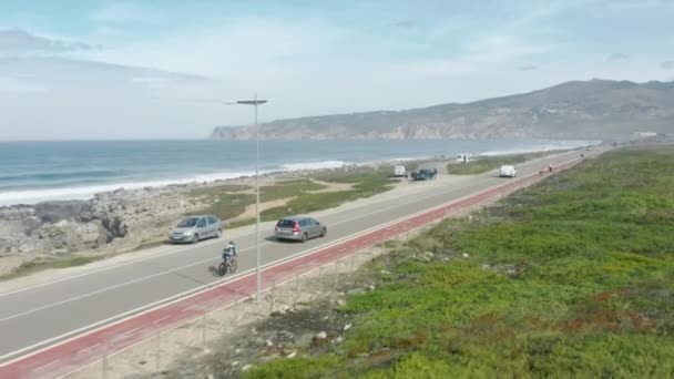 해변을 따라 달리는 차량 가까이에서 자전거를 타고 가는 사람들의 모습 — 비디오
