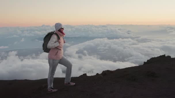 Gelukkig vrouw met rugzak wandelen omhoog schilderachtige vulkanische berg piek bij roze zonsondergang — Stockvideo