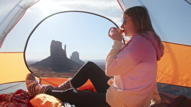 Mujer acampada sentada en tienda de campaña, chica de cámara lenta bebiendo té en Monument Valley — Vídeo de stock