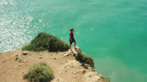 Impresionante vista de un hombre de pie sobre una roca con el océano detrás — Vídeo de stock