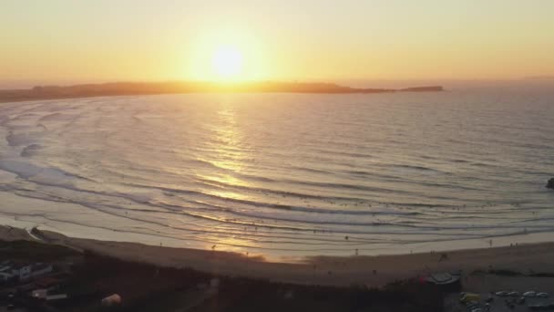 Arka planda sörfçülerin olduğu kıyı günbatımının hava manzarası — Stok video