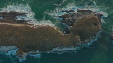 Yeşil deniz dalgalarıyla yıkanmış kayalık oluşumun havadan görüntüsü.
