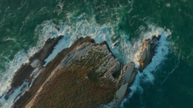 Köpüklü dalgaların yerel yeşilliklerle kaplı bir uçurumu yıkadığı drone görüntüleri.