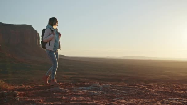 女性ハイカーは日の出に映画の山の崖と赤い砂漠を歩く — ストック動画