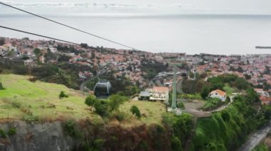 Etrafı yeşil yemyeşil bahçelerle çevrili metal halat boyunca giden araçlar.