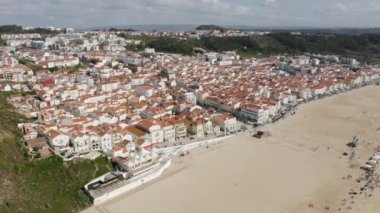 Arkasında yeşil tepeler olan bir sahil bölgesinin hava görüntüleri.