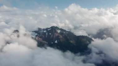 Mavi gökyüzünde hareket eden beyaz bulutlar, yüksek dağların üzerinde uçan dronlar.