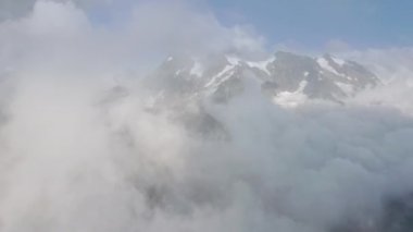 Kışın karlı dağ zirvesini kaplayan beyaz bulutlar arasında destansı bir uçuş.