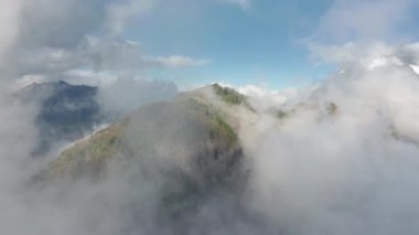 Yoğun bulutlarla kaplı devasa dik dağdaki yeşil ormanın üzerindeki hava manzarası.