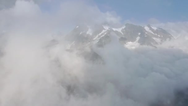 Voo aéreo épico através de nuvens brancas cobrindo cume de montanha nevada no inverno — Vídeo de Stock