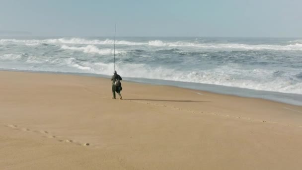 Visser vangt vis met een hengel terwijl hij op het zandstrand staat — Stockvideo