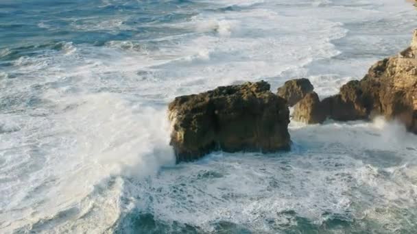 Büyük köpüklü dalgalar yukarıdan görüldüğü gibi kayalık bir sahile çarpıyor. — Stok video