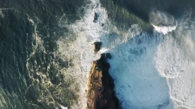 Köpüklü dalgalarla çevrili kayalık oluşum manzarası.