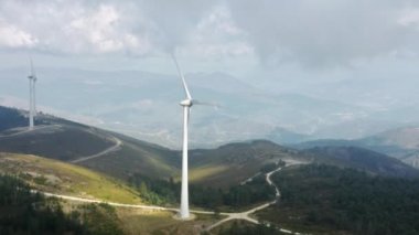 Dağ manzarasında rüzgarla dönen yel değirmeni. Rüzgar türbini enerji üretiyor