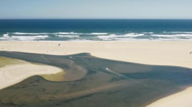 Geniş kumlu alanda yürüyen bir sörfçünün hava görüntüleri.