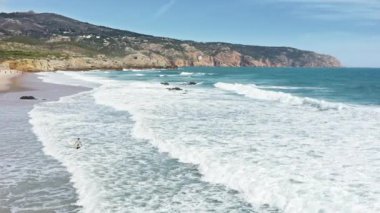 Sörf tahtası olan sporcu antrenmandan sonra kumsala çıkıyor.