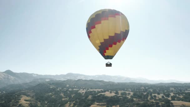 Kleurrijke hete lucht ballon epische vliegen in de blauwe lucht met bergen op de achtergrond 4K — Stockvideo