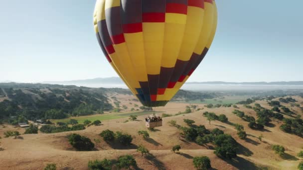 Veelkleurige heteluchtballon met blije enthousiaste toeristen in mand in blauwe lucht — Stockvideo