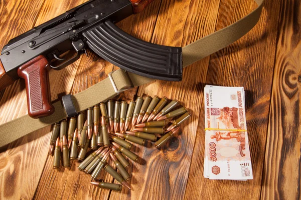 Rifle Kalashnikov e rublos russos na mesa — Fotografia de Stock