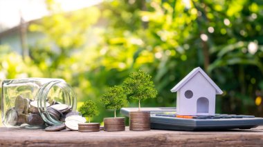 Hesap makinesindeki model ev ve kredi konsepti paralarının üzerinde büyüyen ağaç. Gayrimenkul, Finans, İpotek, Konut Gayrimenkul