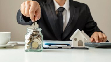 İş adamı tasarruf şişesine ve ev modeline para koyuyor, finansal konsept. Konut kredisi ve Konut kredileri