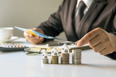 İş adamı madeni konsept ev modelinin olduğu madeni paraların üstüne para koyuyor. İpotek ve Gayrimenkul İpoteği
