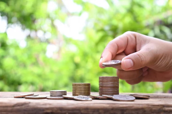 Human hands holding coins and piles of coins on wooden floor financial and investment ideas.