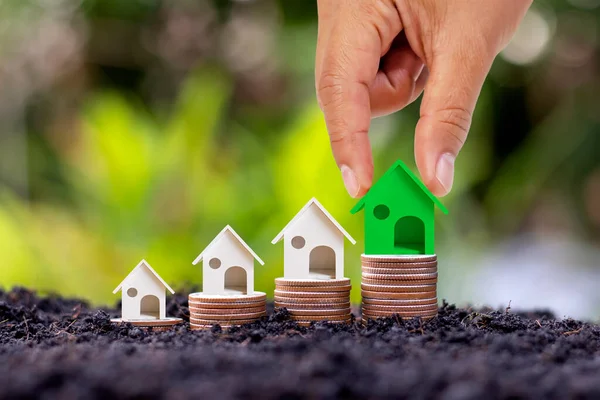 Hand holding green small house model placed on the pile of investment real estate concept coins