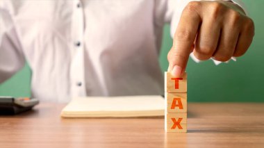 Vergi sözcüğünün yazılı olduğu tahta bir küp tutan genç bir kadın. Finansal kavram. Mali Yönetim ve Vergi Planlama